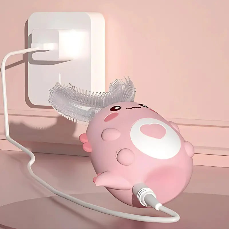Pink dinosaur-shaped children's U-shaped electric toothbrush plugged in and charging against a pink wall.